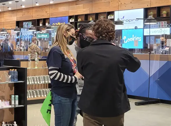Two customers being served at a dispensary counter.