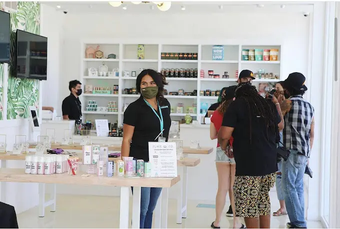 A staff member at a FLWR CO product table with customers browsing behind.